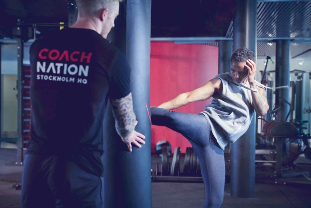 Séance de kickboxing en salle avec un coach guidant une cliente lors d’un exercice sur sac de frappe.